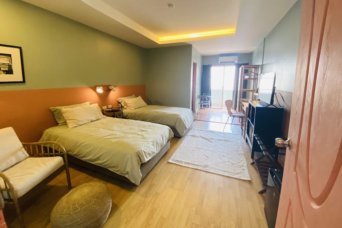 Quarto de hotel com duas camas, uma escrivaninha, uma cadeira e uma pequena mesa.