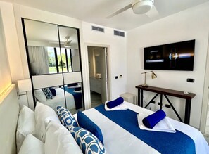 Une chambre d’hôtel avec un lit, un téléviseur fixé au mur, un bureau et un miroir qui reflète la pièce.