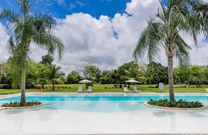 Une piscine entourée de palmiers et de verdure, avec des chaises longues et des parasols.