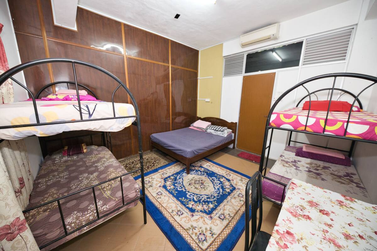 A dormitory room with bunk beds, a wooden wardrobe, a patterned rug, and an air conditioning unit.