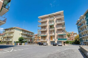 A multi-story residential building with balconies, a parking area, and a clear blue sky. - Il Rifugio - Town Center Apartment With Balcony (Borghetto Santo Spirito)
