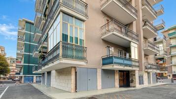 Un edificio residenziale a più piani con balconi, ampie finestre e un ingresso chiuso da cancello.
