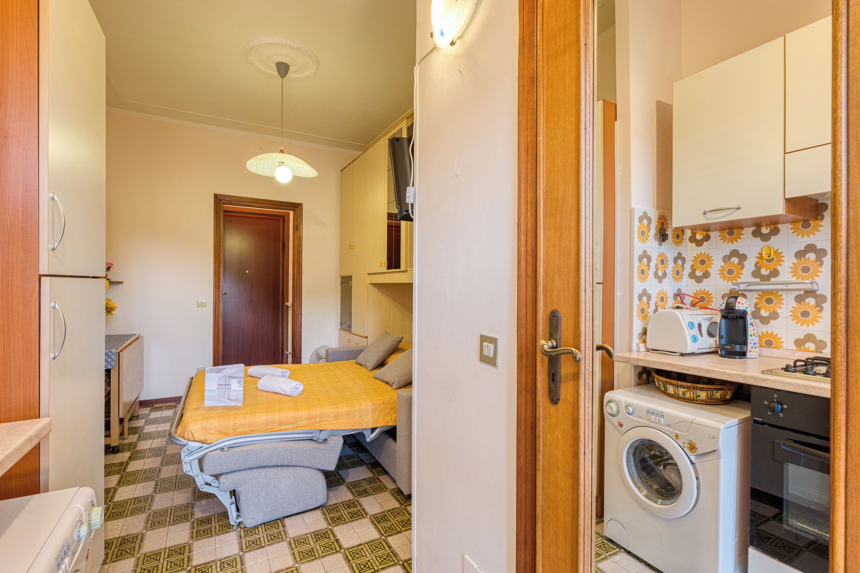 Une chambre d’hôtel de taille réduite, équipée d’un lit, d’une machine à laver et d’une kitchenette.