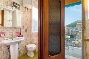 A bathroom with a sink, toilet, and a view of a balcony with outdoor furniture. - Il Rifugio - Town Center Apartment With Balcony (Borghetto Santo Spirito)