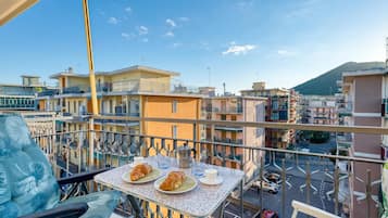 Un balcone con un tavolo apparecchiato per due, due croissant, una tazza e una caffettiera.