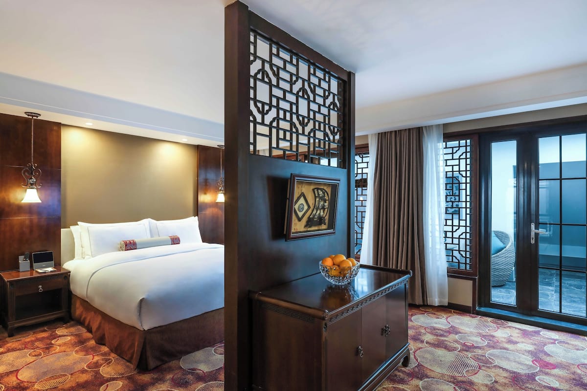Habitación de hotel con cama, mesita de noche, lámpara y un separador decorativo.