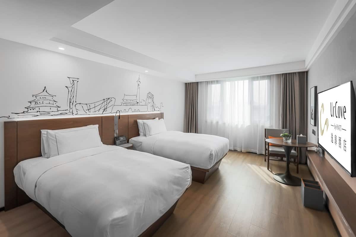 Habitación de hotel con dos camas, un escritorio, una silla, un televisor y un mural en la pared.