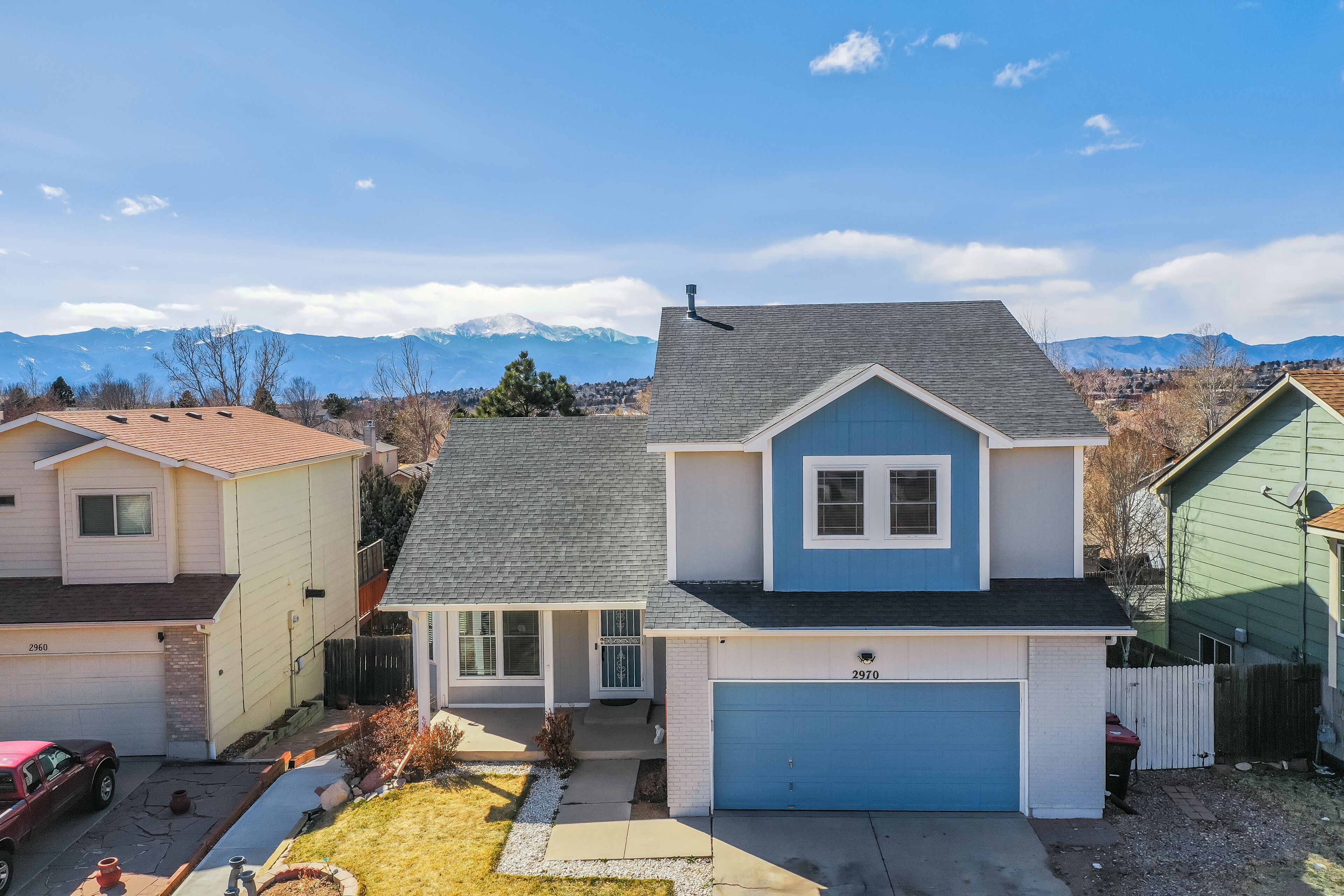 A two-story house with a garage, a front yard, and a mountain backdrop.