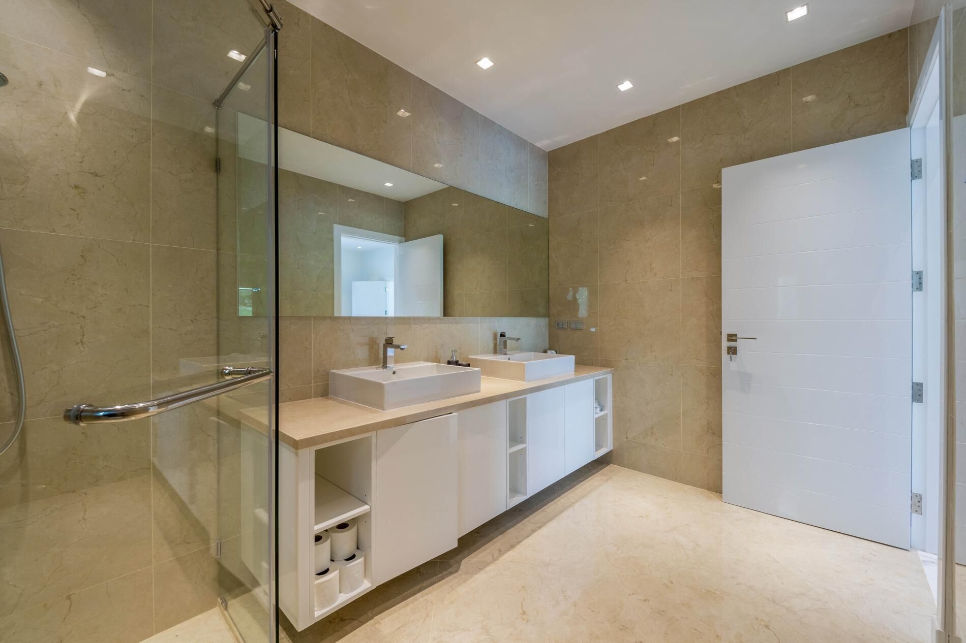 Une salle de bain moderne dotée d’une douche à l’italienne avec paroi en verre, d’un grand miroir, de deux vasques et d’une douche à l’italienne.