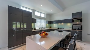 Una cocina moderna con armarios oscuros, una isla grande y un bol de fruta.