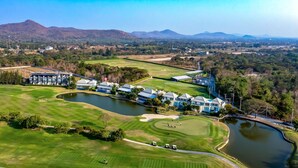 Un campo de golf con un lago, rodeado de edificios residenciales y montañas al fondo.