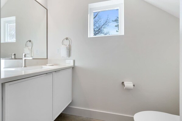 Une salle de bain moderne avec un meuble-lavabo blanc, un grand miroir, une fenêtre et des toilettes.