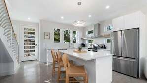 Una cocina moderna con una isla central, electrodomésticos de acero inoxidable y una escalera a la izquierda.