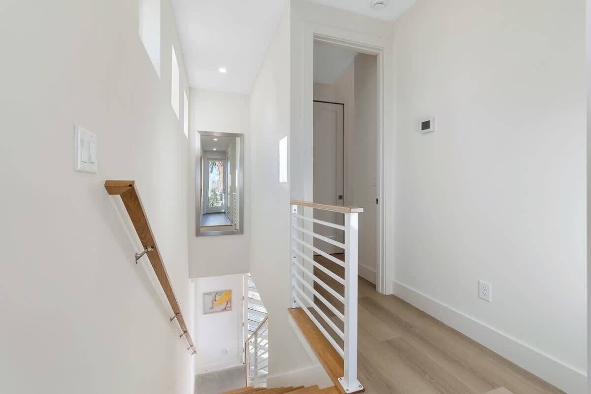 A clean, modern staircase with a wooden handrail and white railings, leading to a bright hallway with a door at the end.