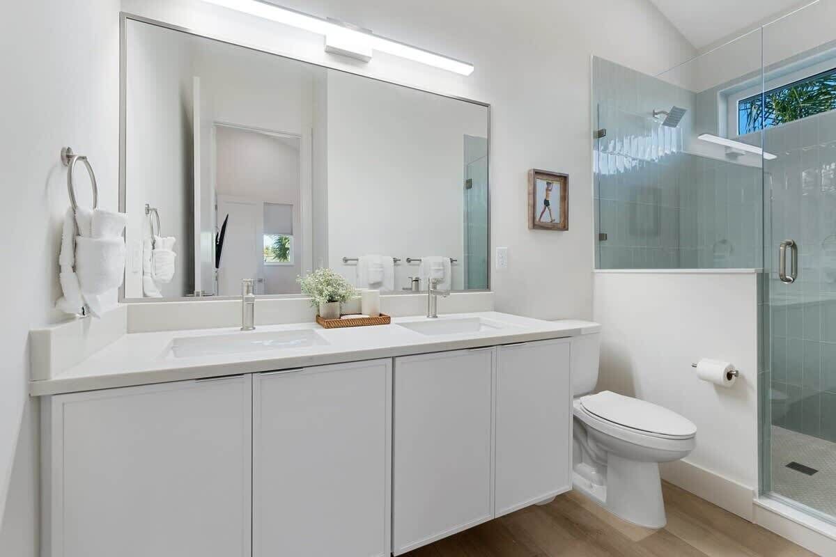 Une salle de bain moderne avec un grand miroir, deux lavabos, des toilettes et une douche à parois de verre.