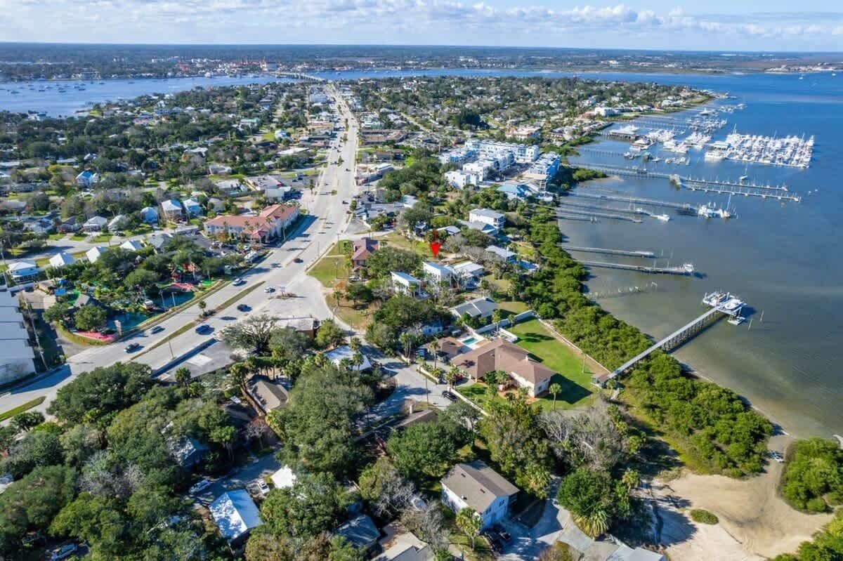 An aerial view of a coastal town with residential areas, a marina, and a long pier extending into the water.