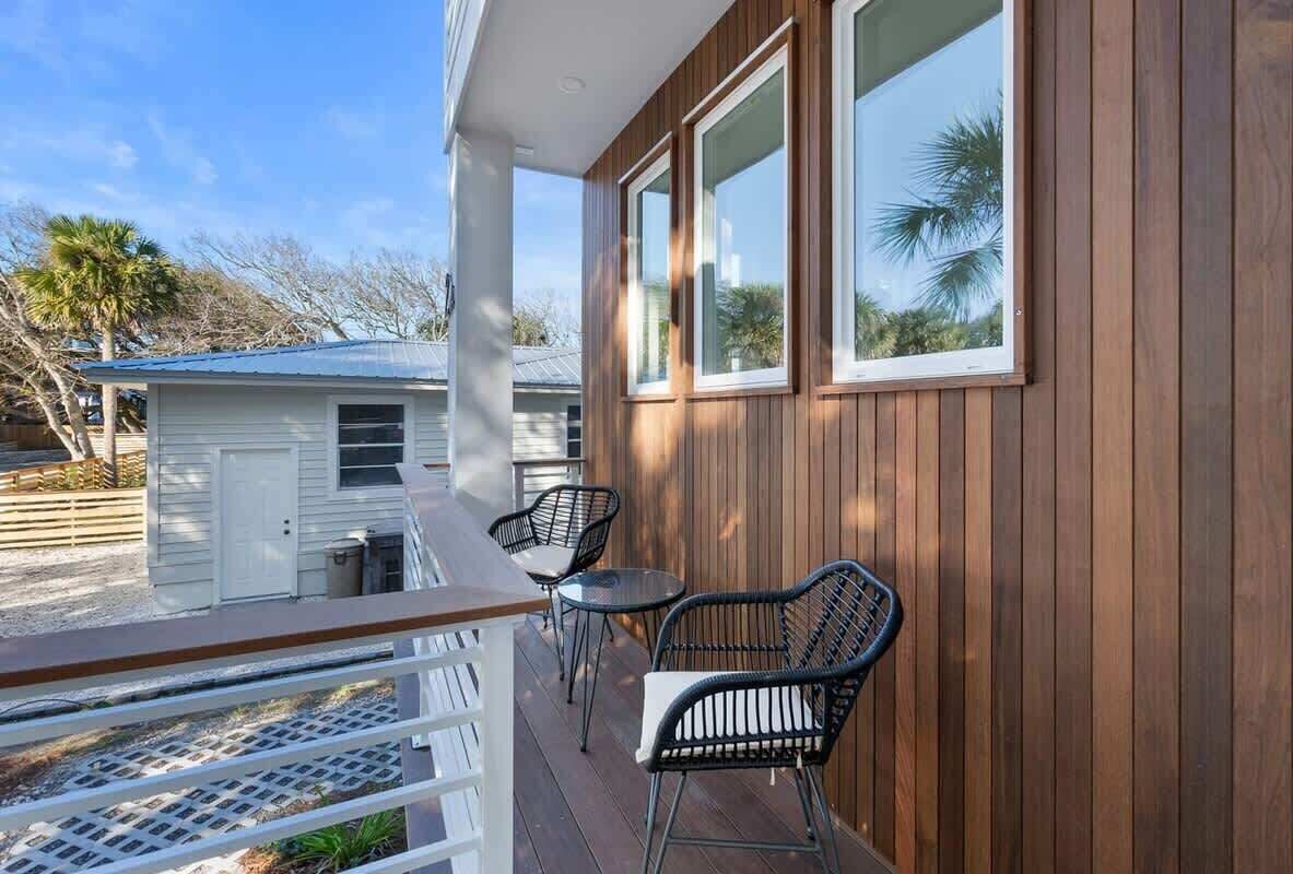 A wooden exterior with a balcony, two chairs, and a small shed in the background.