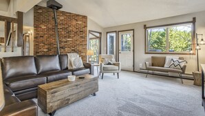 En rummelig stue med en murstensvæg, en brun lædersofa, et træsofabord og en beige lænestol.