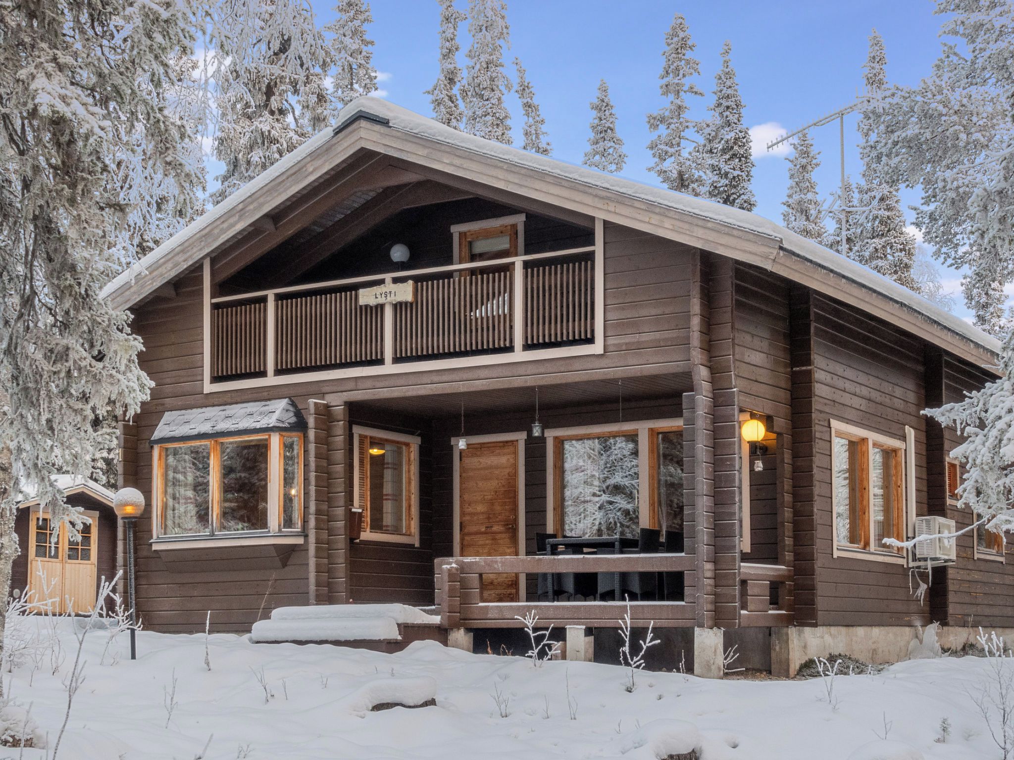 Een houten chalet met twee verdiepingen, een balkon, grote ramen en een overdekte veranda.
