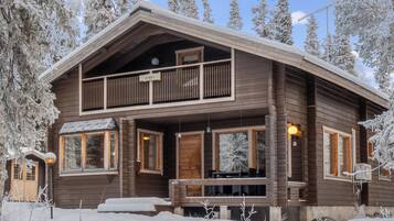 Een houten chalet met twee verdiepingen, een balkon, grote ramen en een overdekte veranda.