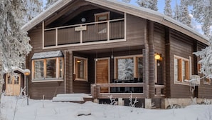 A two-story log cabin with a balcony, large windows, and a snow-covered landscape.