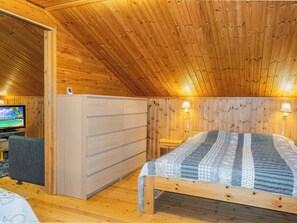 Quarto de madeira com uma cama, uma televisão e uma escrivaninha.
