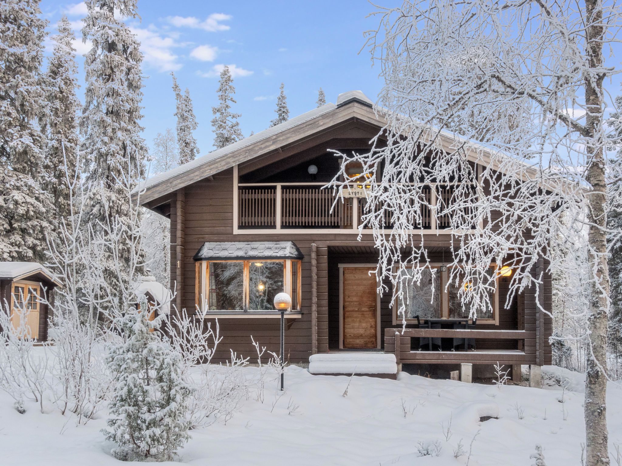 A wooden cabin with a balcony, surrounded by snow-covered trees.