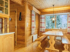 A wooden cabin interior with a dining table, benches, a window with curtains, and a hanging light fixture. - Vacation home Lysti by Interhome (Salla)