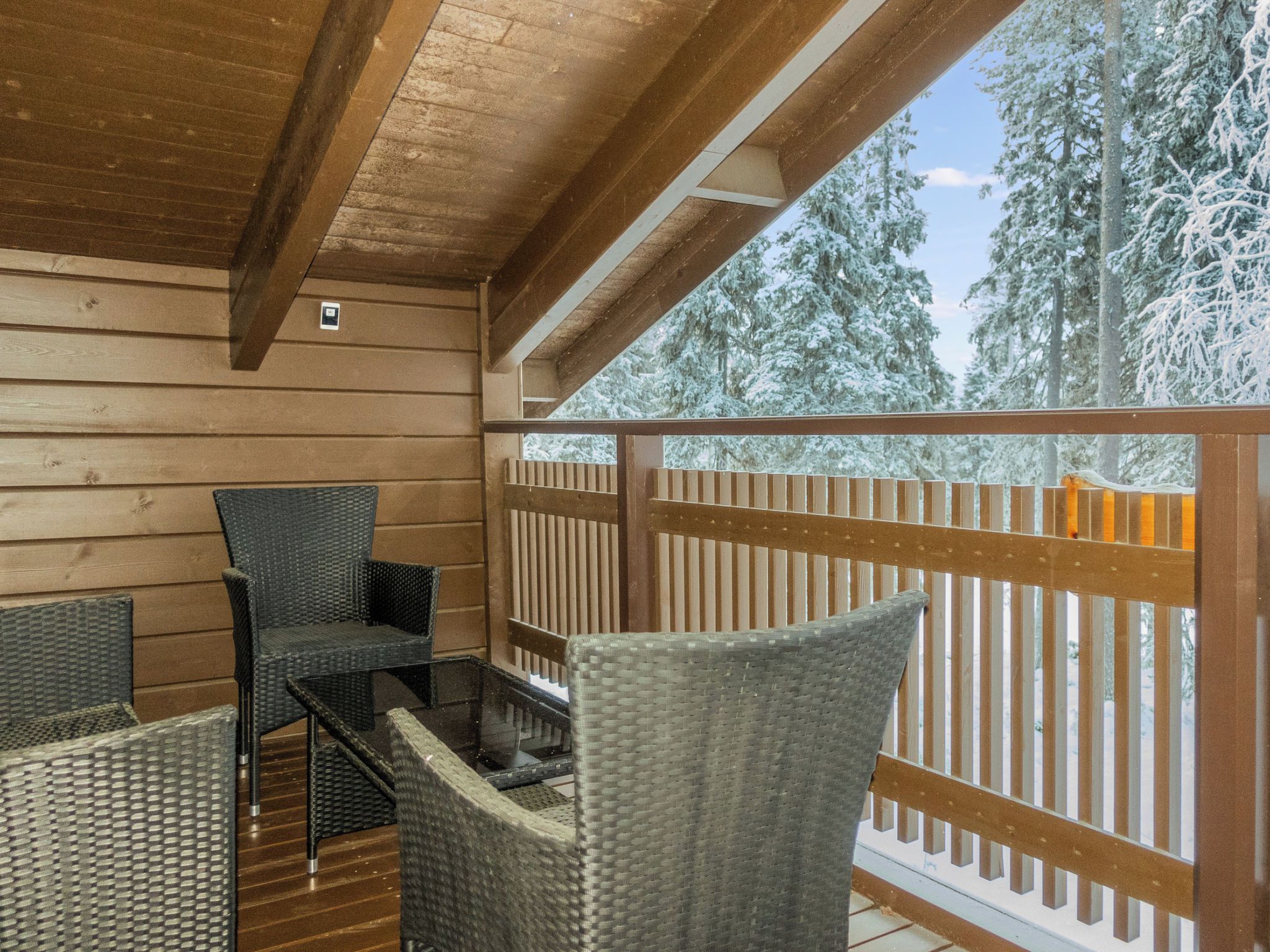 A wooden deck with wicker furniture and a view of snow-covered trees.