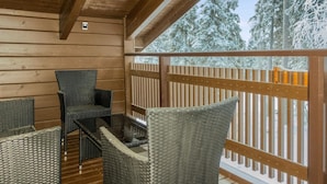 A wooden deck with wicker furniture and a view of snow-covered trees.