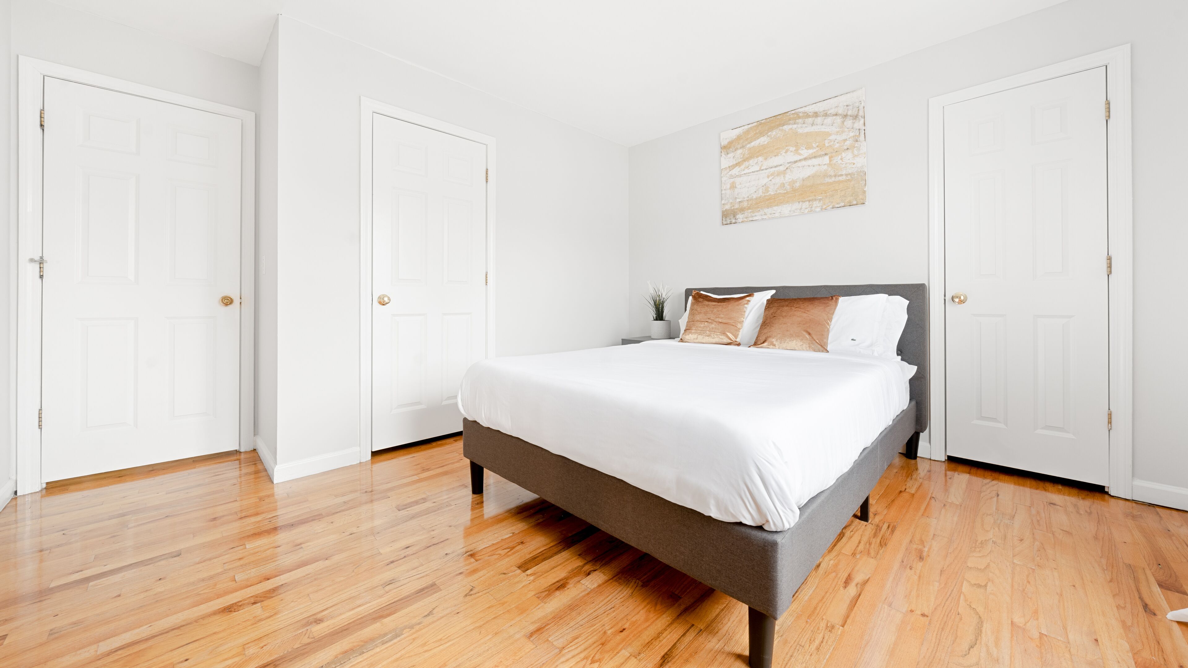Une chambre à coucher avec un lit, un plancher en bois, des murs blancs et deux portes blanches.