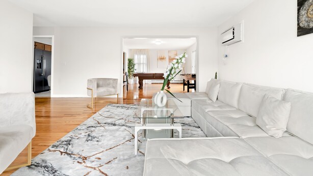 Een moderne woonkamer met een witte bank, een glazen salontafel en een vloerkleed met een marmer dessin.