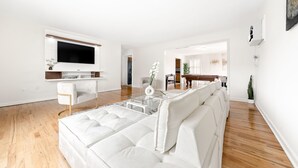 Een moderne woonkamer met een witte bank, een glazen salontafel en een flatscreen televisie aan de muur.