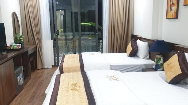 Habitación de hotel con dos camas, televisión, escritorio y balcón con cortinas.