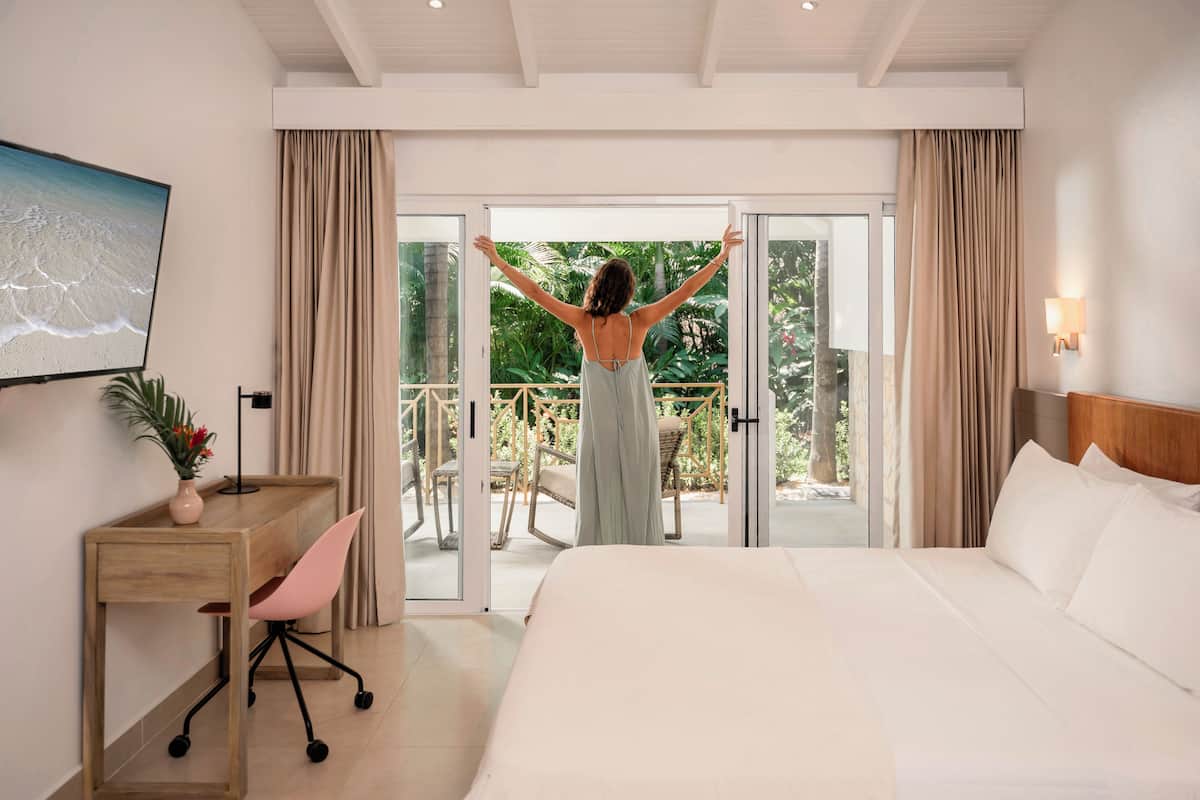 Een hotelkamer met een bed, een bureau met stoel, een televisie en een balkon met gordijnen.