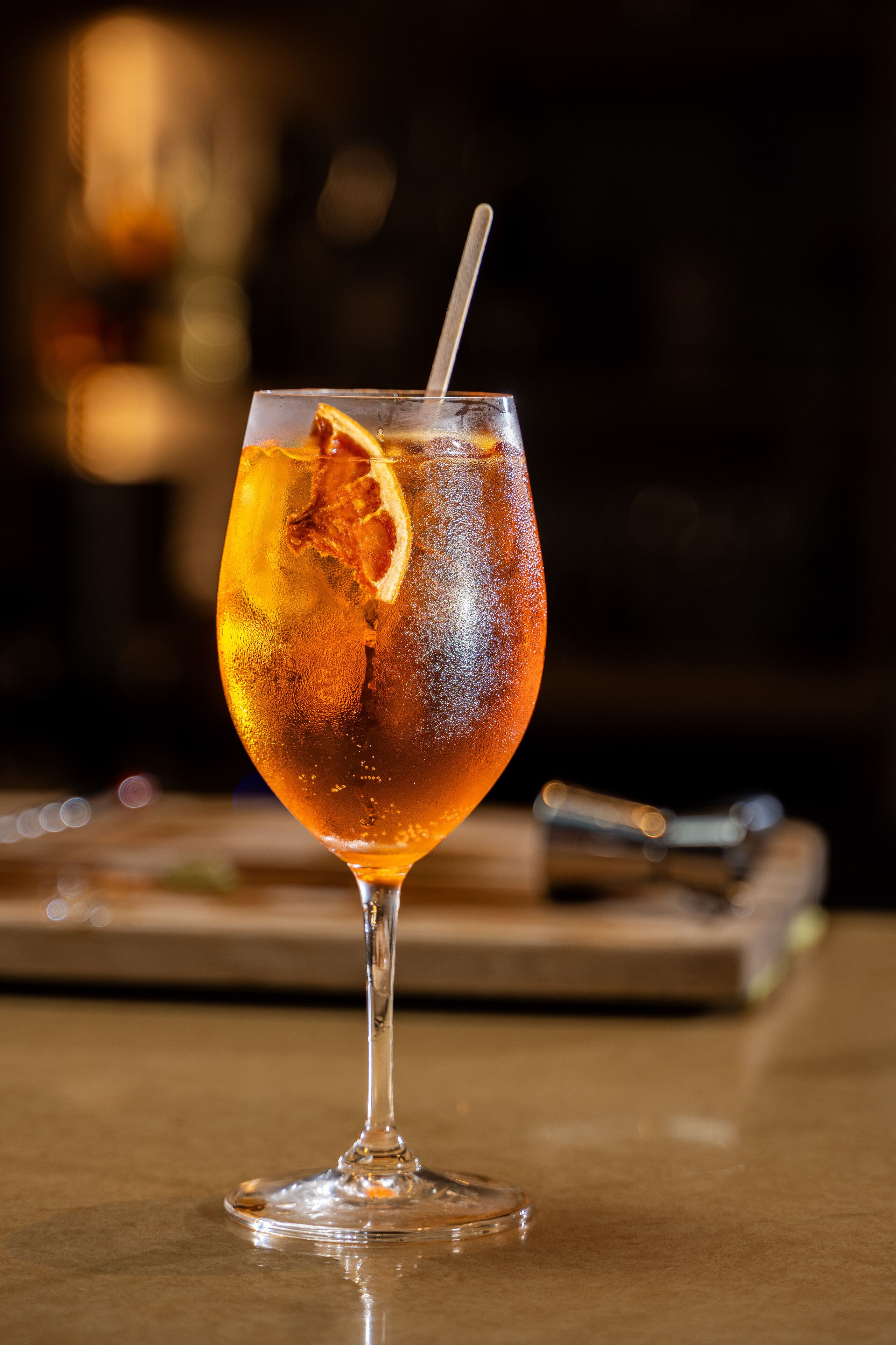 A clear glass with a straw and a slice of orange on a table.