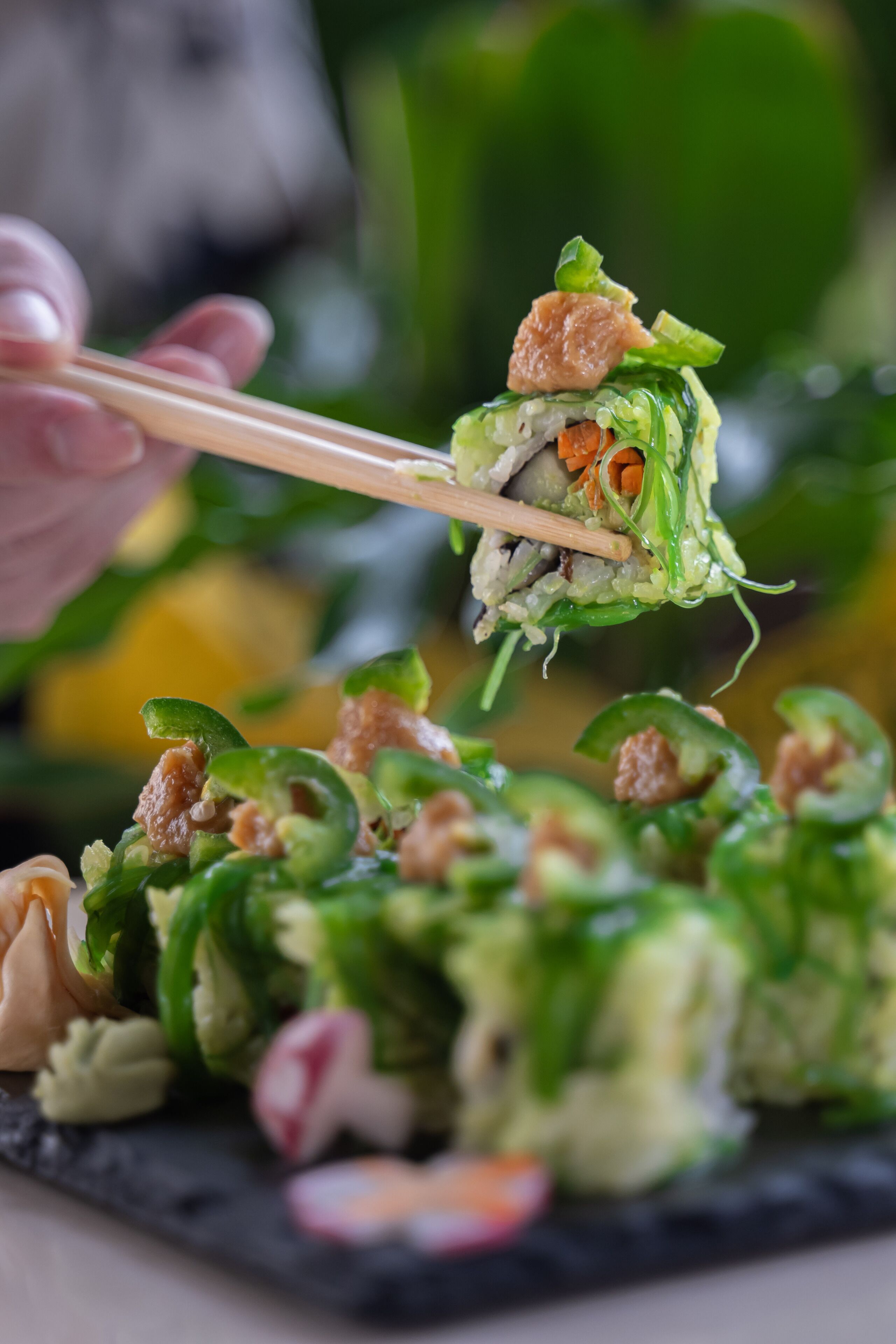 A close-up of a dish with green vegetables and meat, held by chopsticks.