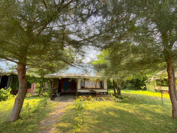 A small, rustic house with a porch, surrounded by lush greenery and trees. - Rickys Beach House (Koto XI Tarusan)