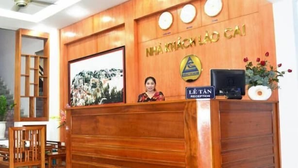 A reception desk with a wooden finish, a framed picture above it, and a sign that reads "NHÃ KHÃCH LAO CAI". - Lao Cai Hotel by Bay Luxury (Hanoi)