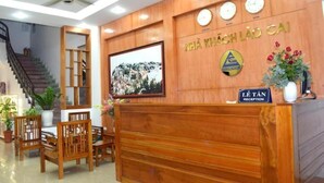 A reception area with a wooden reception desk, a framed picture on the wall, and a staircase in the background. - Lao Cai Hotel by Bay Luxury (Hanoi)