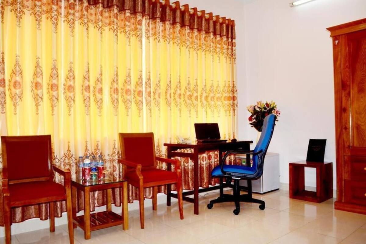 A room with a desk, two red chairs, a laptop, a blue office chair, a small table with a vase of flowers, and a wooden cabinet.