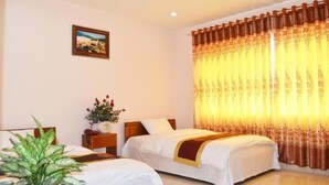 A hotel room with two beds, a nightstand with a vase of flowers, a framed picture on the wall, and a large window with curtains. - Lao Cai Hotel by Bay Luxury (Hanoi)