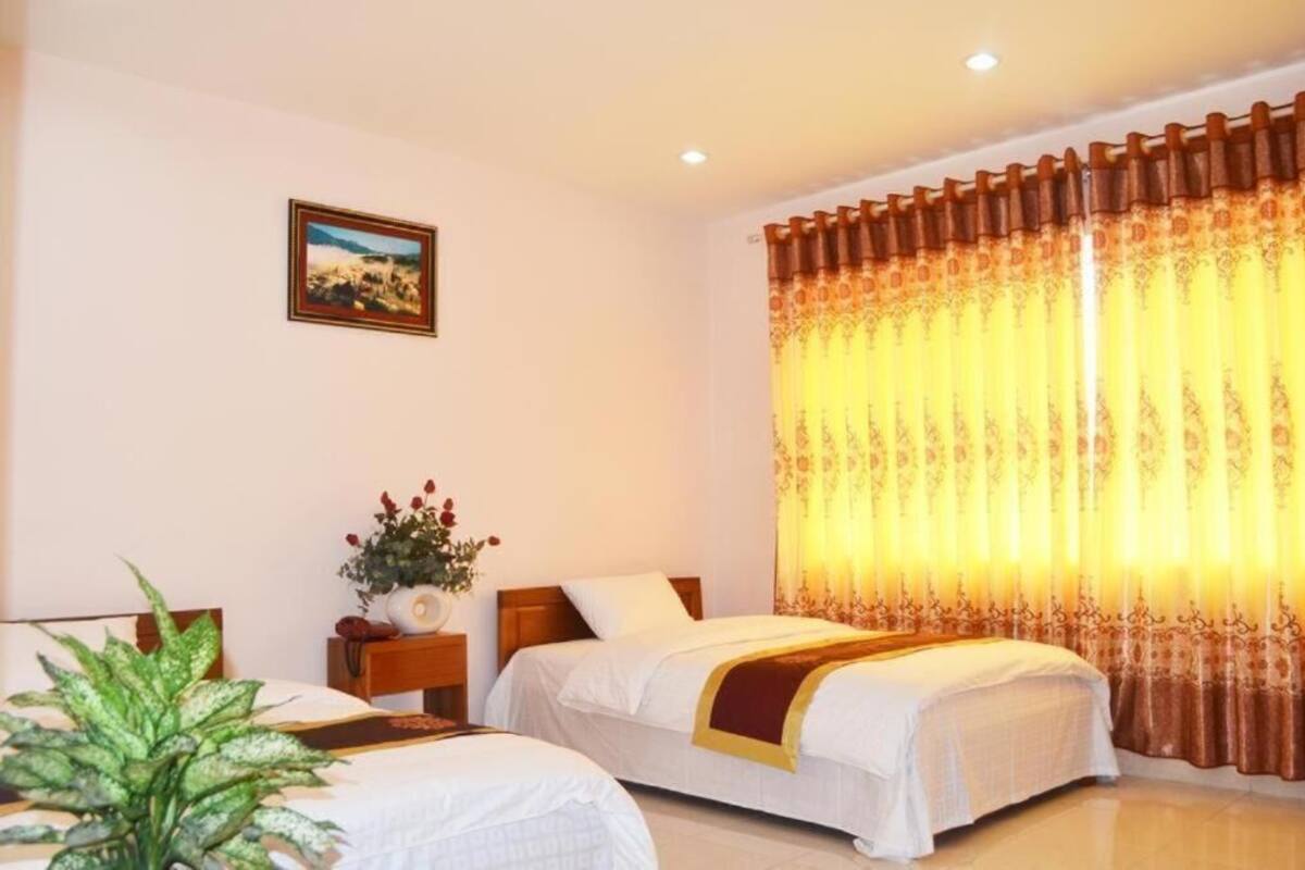A hotel room with two beds, a nightstand with a vase of flowers, a framed picture on the wall, and a large window with curtains.