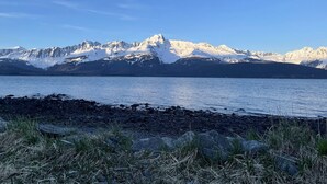 Ein See mit steiniger Uferlinie und schneebedeckten Bergen im Hintergrund.