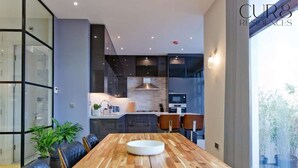 Uma cozinha moderna com armários escuros, uma ilha central e uma área de refeições com mesa de madeira e cadeiras de couro.