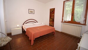 A bedroom with a bed, a nightstand, a chair, a window with curtains, and a radiator. - Luxurious Bungalow in Garda with Swimming Pool (Garda)