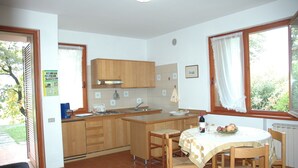 A kitchen with wooden cabinets, a sink, and a dining area with a table and chairs. - Luxurious Bungalow in Garda with Swimming Pool (Garda)