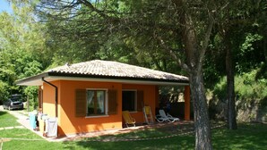 A small orange house with a tiled roof, a covered porch, and a lawn area with two lounge chairs. - Luxurious Bungalow in Garda with Swimming Pool (Garda)