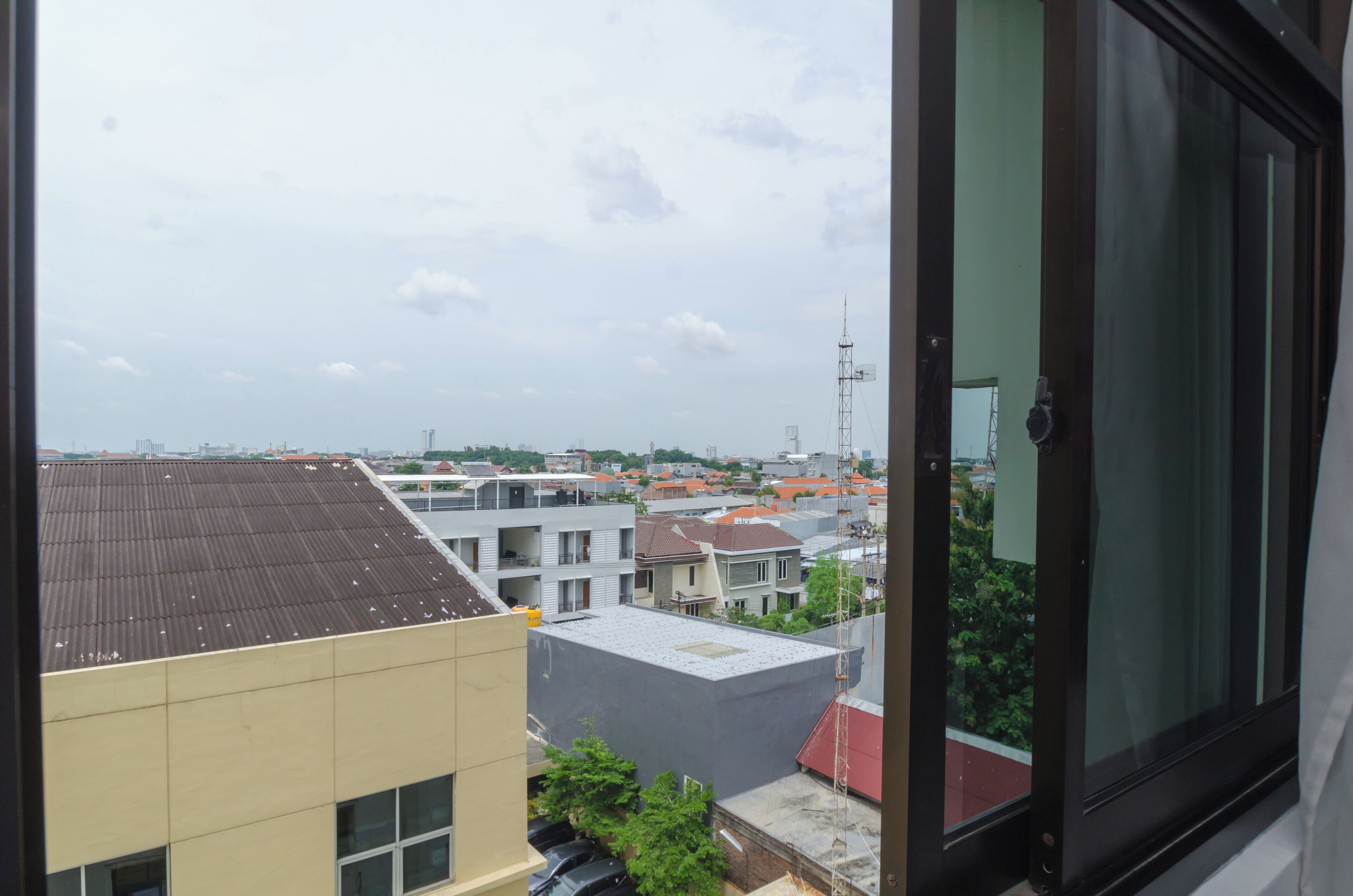 A view from a window overlooking a residential area with various buildings, including a multi-story structure with a flat roof and a smaller building with a sloped roof.