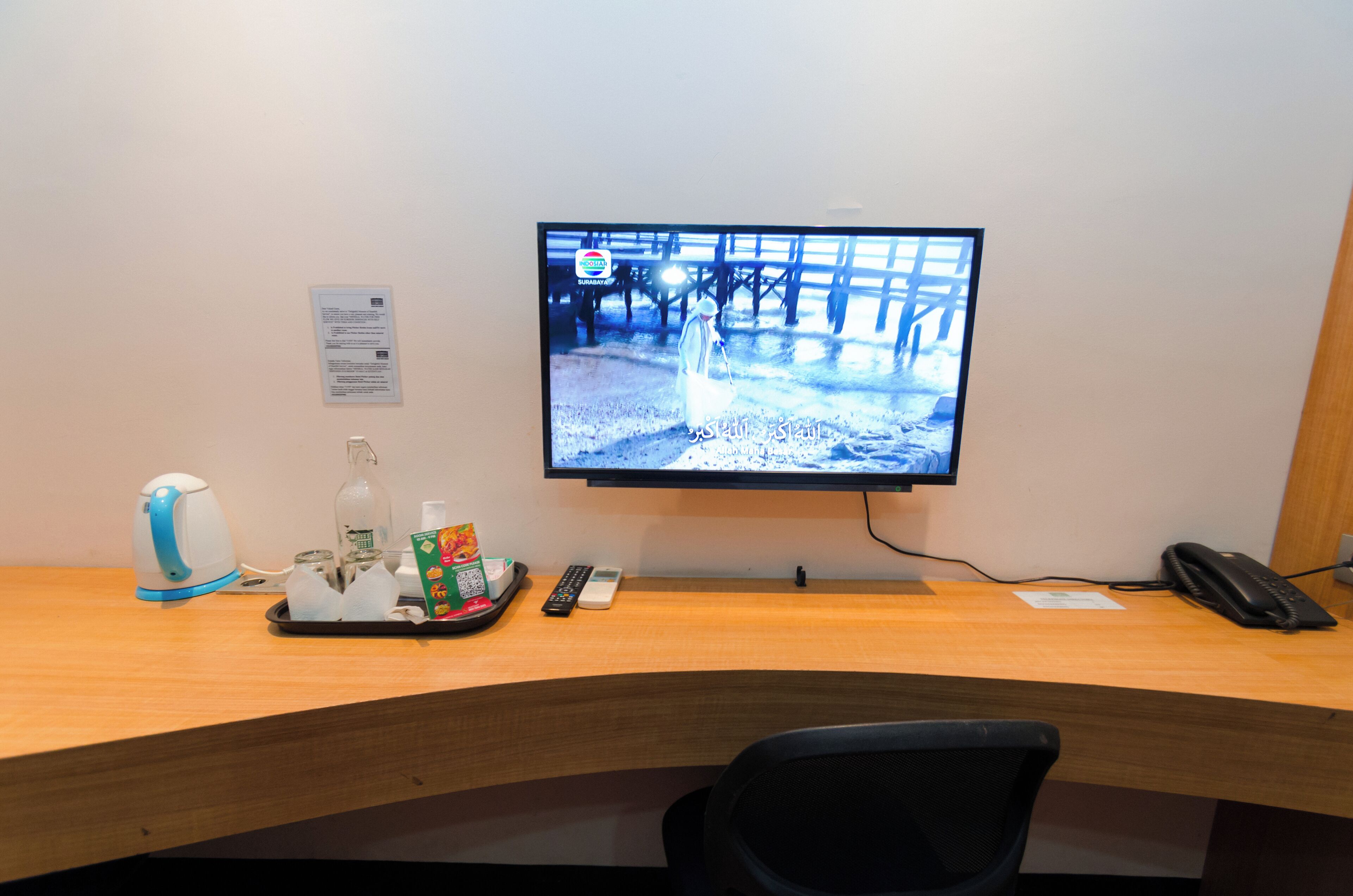 Un bureau avec un écran d’ordinateur affichant un paysage enneigé, une bouilloire, un plateau avec des collations, une télécommande et un téléphone.